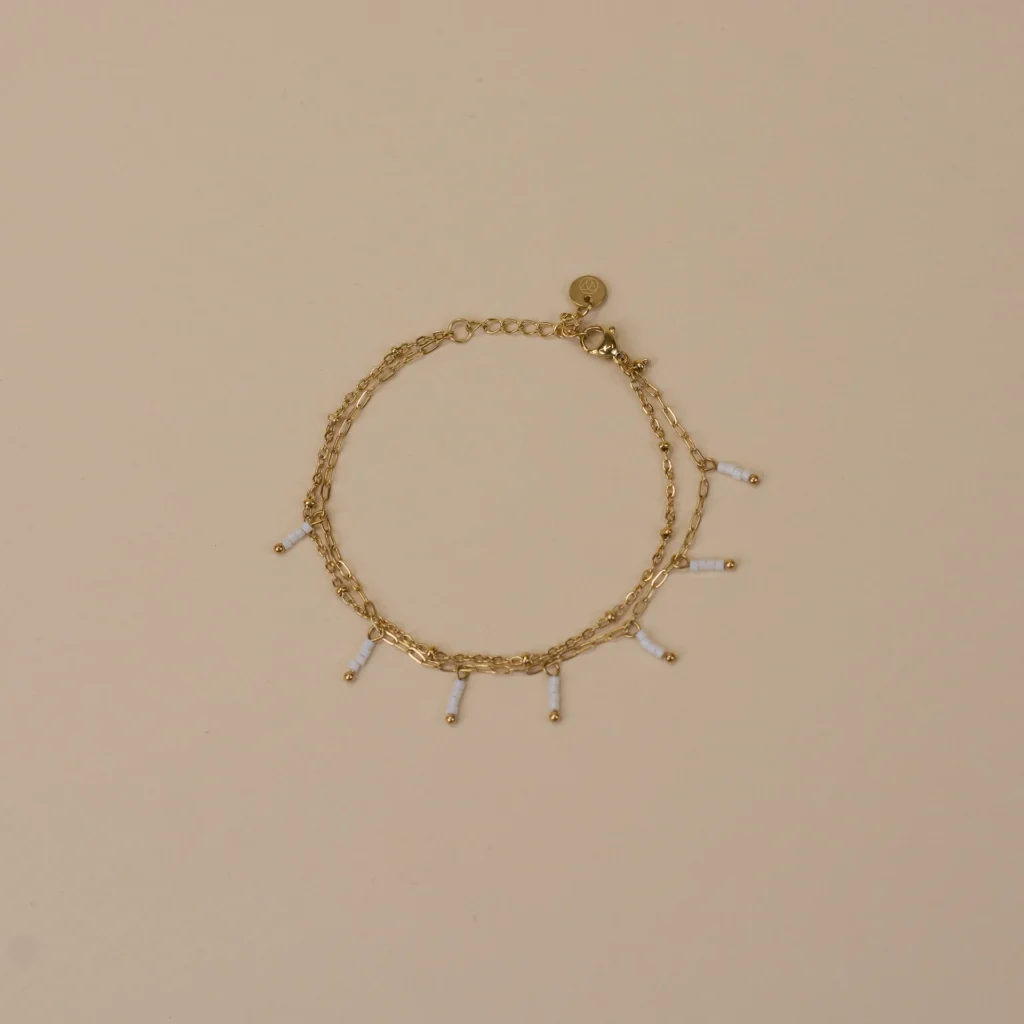 Ivy Bracelet Gold 1 gouden armband met 7 ivoor parelkleurige bedeltjes en gouden knopjes elegant minimalistisch dames sieraad op neutrale achtergrond