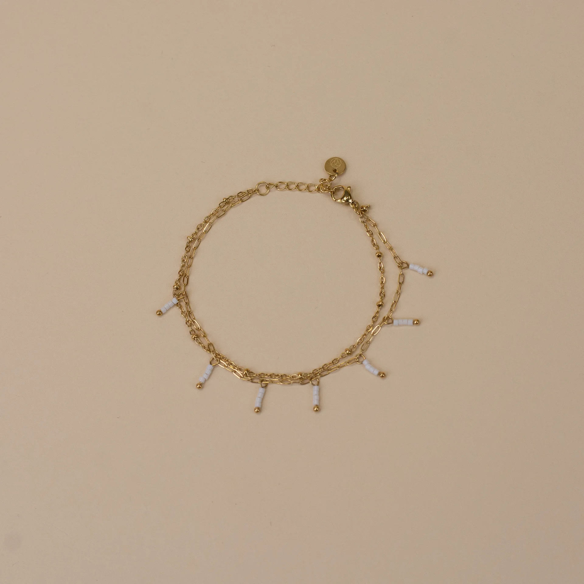 Ivy Bracelet Gold 1 gouden armband met 7 ivoor parelkleurige bedeltjes en gouden knopjes elegant minimalistisch dames sieraad op neutrale achtergrond