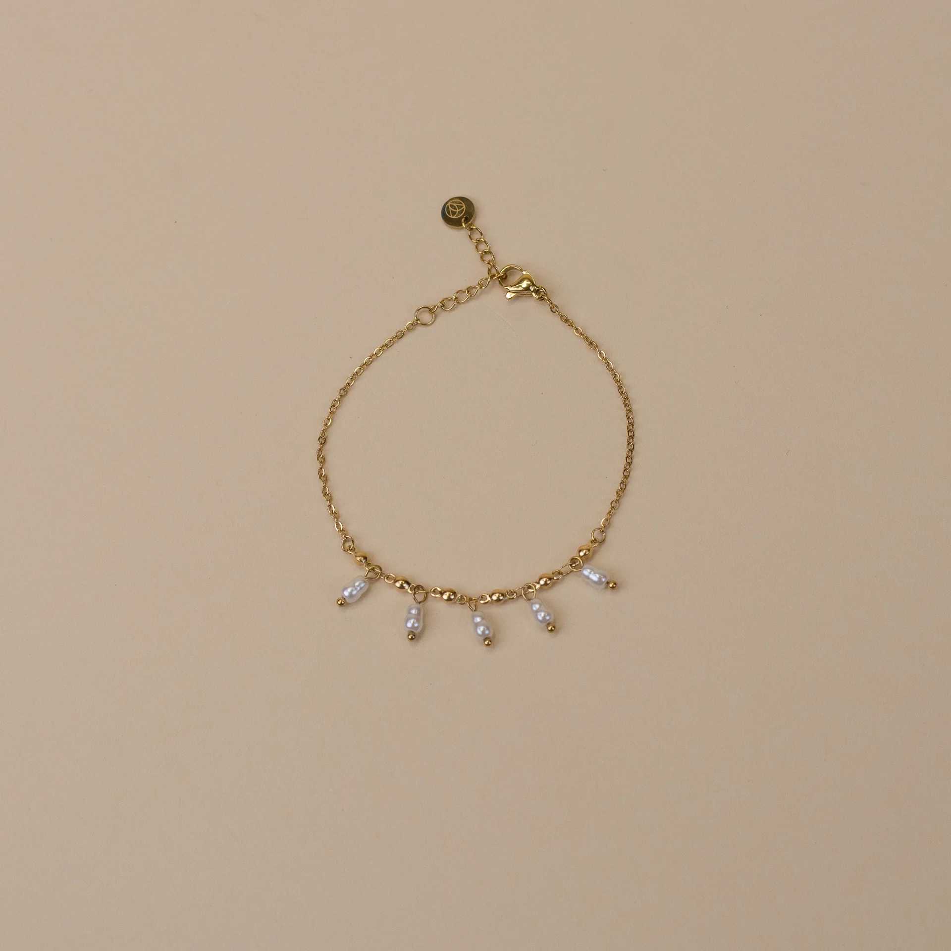 Lola Bracelet Gold 1 gouden armband met vijf parelmoer kleurige bedeltjes minimalistisch sieraad bovenaanzicht op neutrale achtergrond elegante dames armband