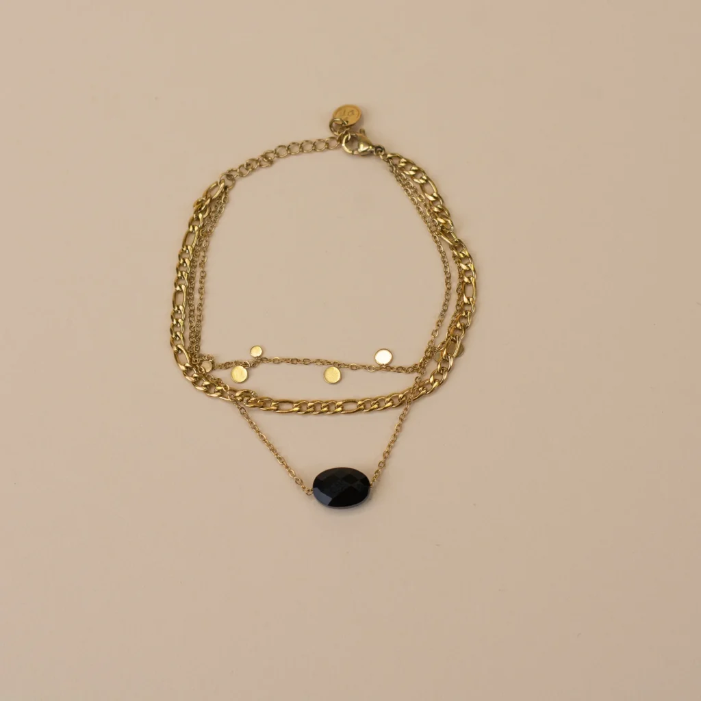 Zoë Bracelet Gold 1 elegante gouden armband met zwart steentje, verfijnd sieraad voor vrouwen gefotografeerd op beige achtergrond uit de Sarae collectie